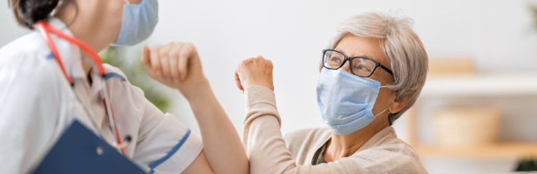 Vacunación Médica chocando codos con una paciente mayor